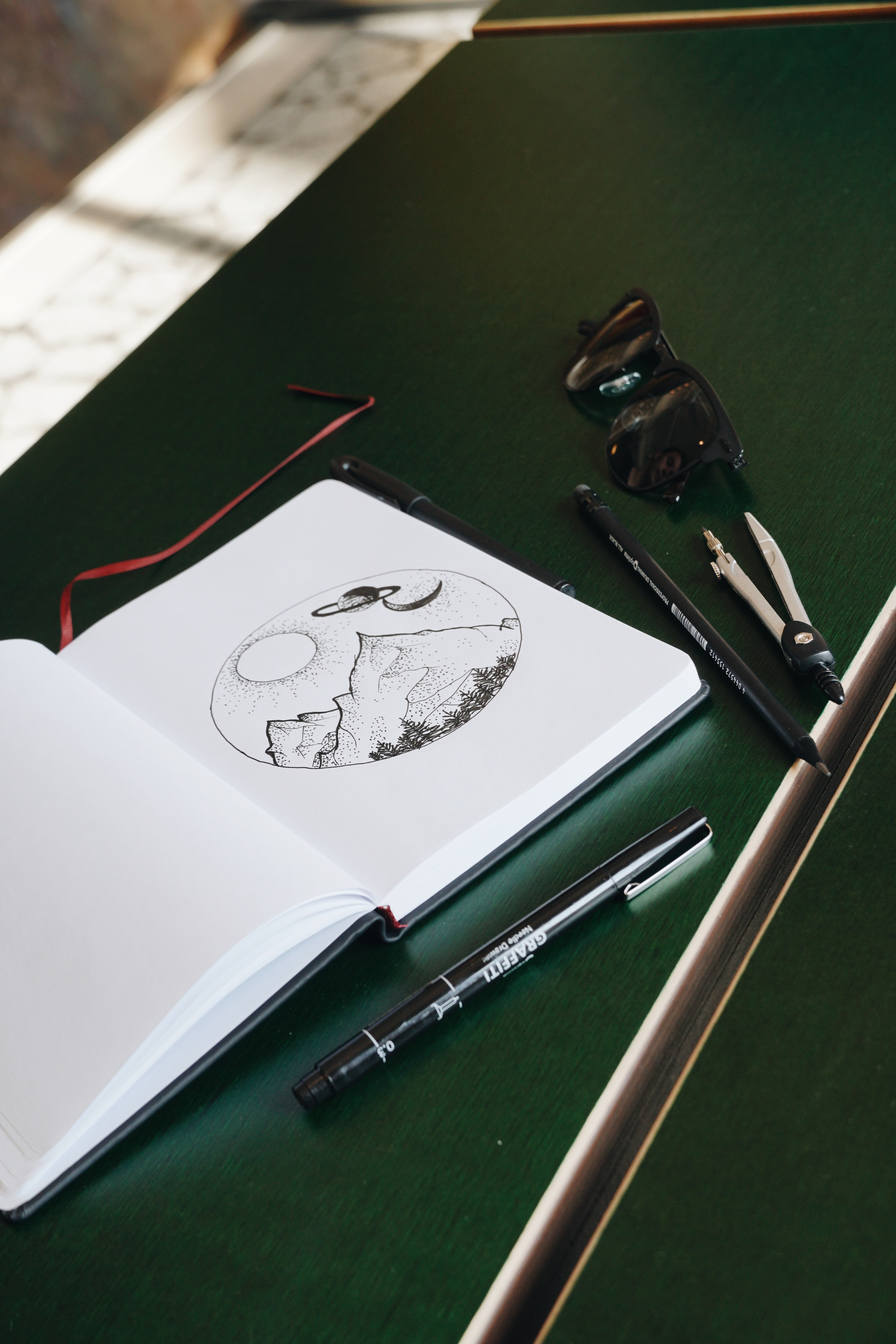 journal with drawings of mountains in a circle, equipment around it on desk